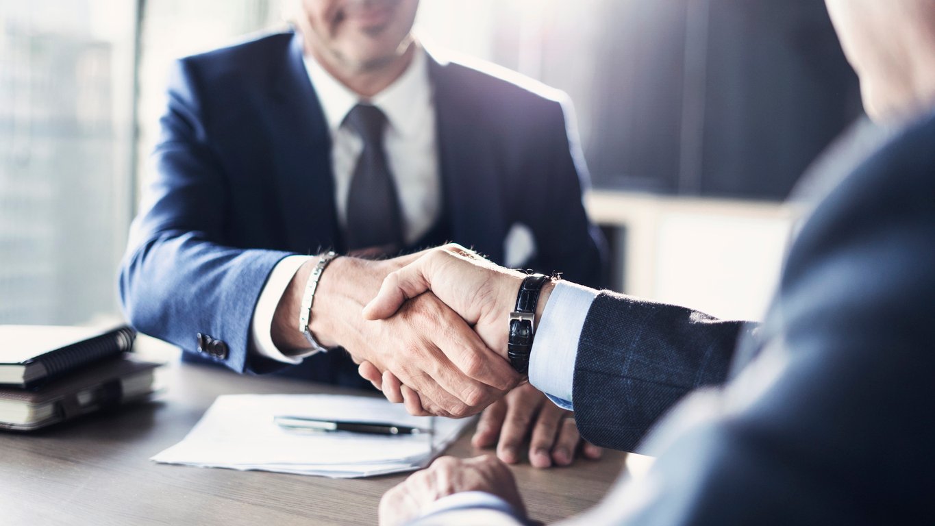 Real estate agent shaking hands with a male real estate broker in an office.